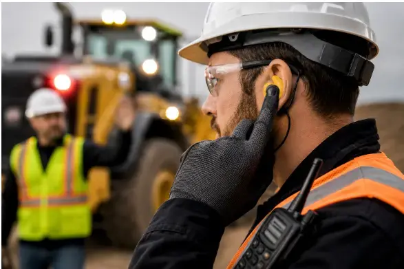 Worker fitting an earplug while working around heavy machinery